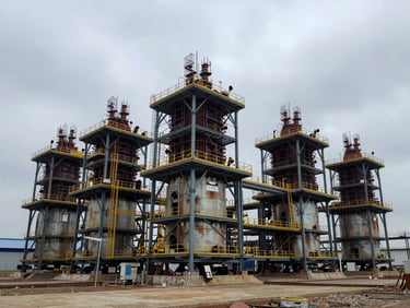 Wide environmental shot of the Tanjung Agas industrial site under overcast daylight, showing heavy infrastructure foundations and steel framing.