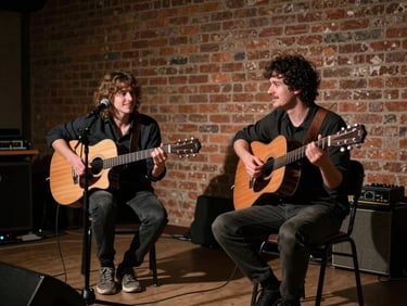 Two musicians seated in a rehearsal space, acoustic guitars on their laps, low-key side lighting casting long shadows, brick wall in background, candid touring camaraderie moment, no posed smiles