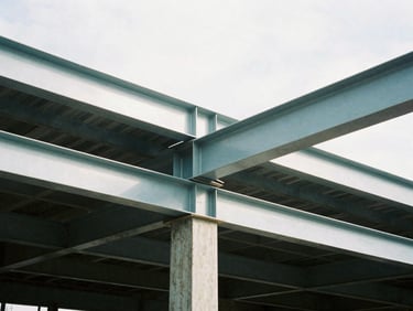 Tight graphic detail of structural steel beams being installed inside an existing building undergoing renovation, hard daylight, high-contrast cool tones, 35mm.
