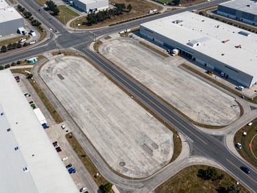 Aerial view of a flat, cleared industrial site near a major highway intersection, showing clean access roads and surrounding logistics warehouses.
