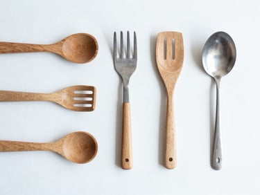 Top-down flat lay of minimalist wooden and steel kitchen utensils on a clean white surface