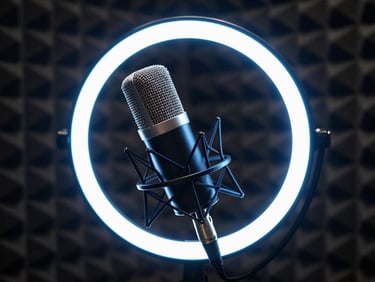 Close-up of a broadcast microphone with a glowing blue ring light in a dark, professional sound isolation booth.