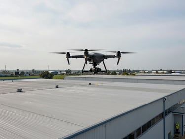 Drone hovering above large industrial warehouse roof, operator visible below in PPE, overcast sky, wide environmental shot showing full roof scale
