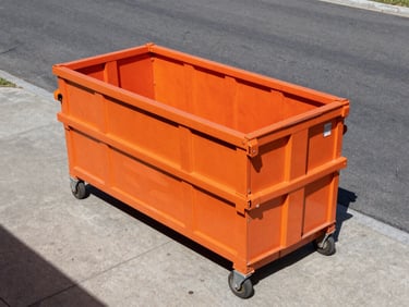 Dynamic low-angle wide-angle shot of a clean empty roll-off dumpster positioned precisely on a concrete driveway, high-contrast daylight, safety orange details, gritty industrial style.