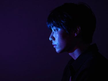 Moody atmospheric shot of a person in deep contemplation, illuminated by a single sharp neon blue light source, deep shadows, 35mm lens