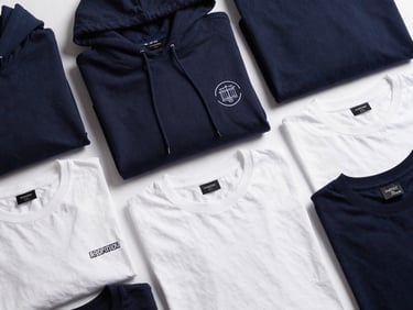 Flat lay of premium customized apparel including embroidered hoodies and printed t-shirts in deep navy and white