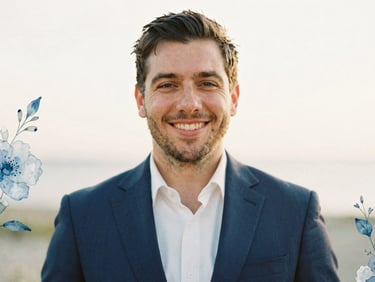 Candid portrait of a smiling man in a navy suit, soft golden-hour light, shallow depth of field, delicate hand-painted blue watercolor floral accents.