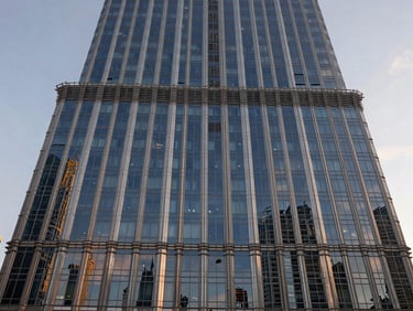 Straight-on architectural facade of a Downtown Dubai tower, floor-to-ceiling glazing reflecting dawn sky, shot at street level looking upward, geometric precision in the curtain wall pattern