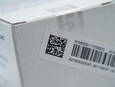Macro close-up of a secure, sealed pharmaceutical box with barcoded tracking label, clinical white studio lighting, sharp 50mm focus