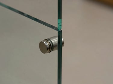 Macro detail of a frameless glass railing panel edge, toughened glass catching ambient light with a subtle green tint along the edge, stainless spigot fitting visible at base