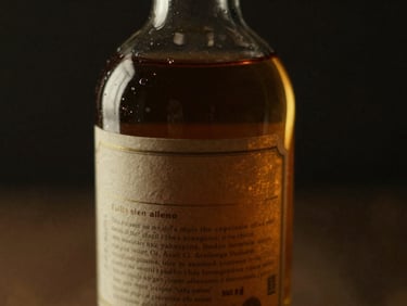 Close-up of a vintage bottle of rare amber spirit, label partially obscured, in a dark, moody setting with golden highlights, shallow depth of field