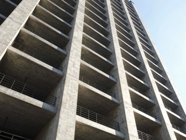 Low-angle architectural shot of concrete pillars and steel beams of a modern high-rise building under high-contrast daylight.
