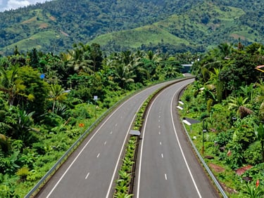 Wide-angle scenic view of a modern highway passing through lush green Kerala landscape, representing infrastructure and connectivity.