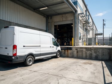 Low-angle dynamic shot of a clean white cargo van parked at a modern concrete warehouse loading dock, bright midday sun, sharp industrial shadows.