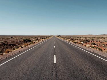 Wide daylight shot of a completed two-lane asphalt road stretching to the horizon across flat Argentine pampa, freshly painted lane markings, road shoulders clear and graded, expansive sky, no vehicles or workers, documentary framing showing full road extent and surrounding landscape