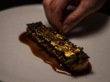 Chef delicately plating a savory dish with a dark golden reduction line, extreme close-up on the texture, moody editorial style
