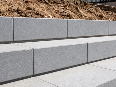 Low-angle shot of a gray engineered retaining wall holding back a clean soil grade, proper drainage backfill visible, sharp daylight.