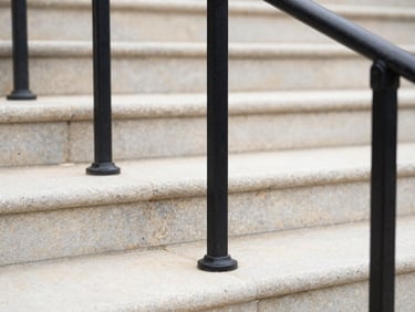 Macro detail of crisp black aluminum handrails mounted on clean limestone steps, natural overcast daylight
