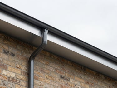 Detailed architectural shot of clean aluminum fascia and seamless dark downspouts on a modern brick facade, overcast sky