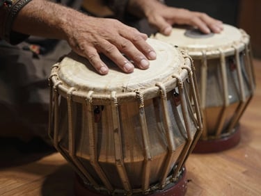 Macro shot of tabla pair, one hand's fingers resting on the bayan skin, soft north-light from above, wooden floor beneath