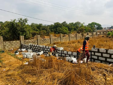 Construction workers in safety vests building a concrete block perimeter wall on a rural property.