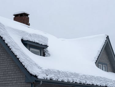 Wide panoramic view from street level looking up at a heavily snow-laden residential roof in Quebec, thick white accumulation pressing down on shingles, overcast harsh winter daylight, no people, dramatic weight of snow visible