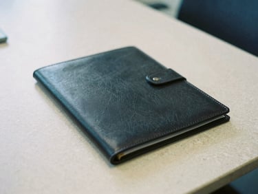 Close-up of a dark leather portfolio folder resting on a minimalist stone conference table, diffused office light.