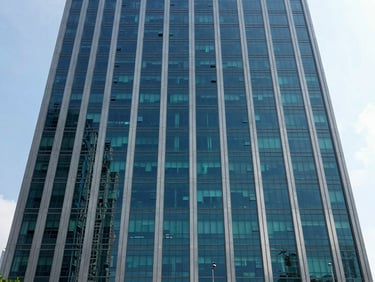 Wide exterior shot of a modern Indonesian high-rise reflecting bright daylight, emphasizing institutional establishment and corporate scale.