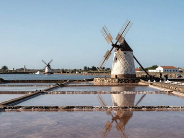 Sunny daylight view of the historic salt pans and traditional windmills of São Pedro da Aldeia next to the calm lagoon.