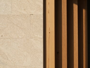Close-up architectural shot of hand-selected travertine stone blocks meeting raw oak panels under soft morning light, straight vertical lines, cinematic framing
