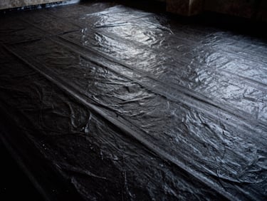 Close-up of sub-grade basement tanking membrane, thick charcoal texture, dramatic low-key highlights.