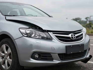Close documentary frame of a sedan's crumpled front bumper and hood after a collision, natural overcast daylight, no people, case-evidence style photography