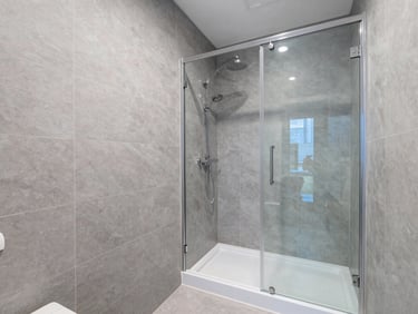 Wide shot of a newly renovated minimalist bathroom with slate grey tiles and a glass shower, bright daylight