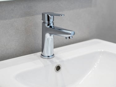 Modern chrome bathroom faucet installed on a clean white ceramic sink, bright natural daylight