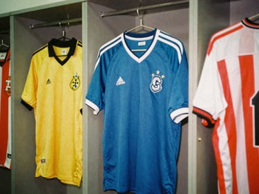 Analog 35mm photo of retro football shirts hanging on a locker room wall, soft natural light, warm saturated colors, heavy grain