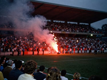 Slightly blurry VHS tape still of a crowded stadium terrace with red flares burning, direct flash, heavy grain, nostalgic 90s aesthetic