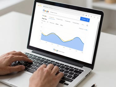 Tight crop of a laptop screen showing Google Search Console performance graphs, hands resting on keyboard, clean desk surface, studio daylight, no decorative objects