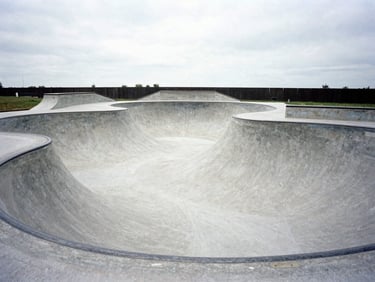 Wide shot of a newly built concrete skate bowl in Antwerp, high-contrast overcast daylight, low-angle, gritty film photography