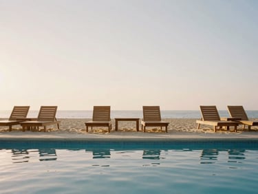 Straight-on architectural elevation of a clean, uncrowded pool deck at golden hour, calm water reflecting the warm sky, minimalist teak lounge chairs.