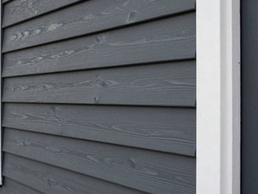 After: the exact same cedar siding, fully sanded, primed, and finished in a solid dark slate gray with crisp white trim.