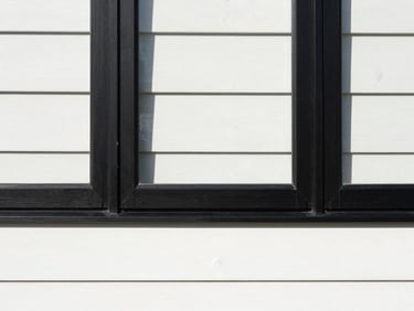 Straight-on architectural detail of a newly installed black window frame against clean white siding, crisp paint line, direct daylight.