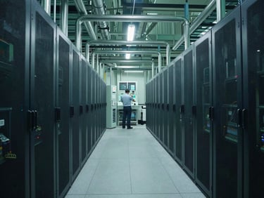 Wide shot of a modern data center cooling plant, visible pipes and chillers, cool industrial lighting, engineer reviewing a control panel in the mid-ground.