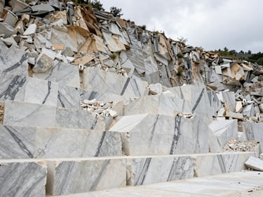 Wide environmental view of an Apuan Alps marble quarry face in northern Tuscany, raw Calacatta blocks extracted from pale cliff, overcast diffused light showing true white-grey stone colour, no people visible