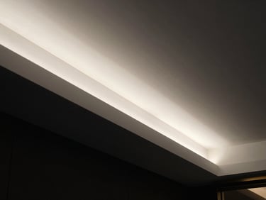 Close-up of a flawless white plaster false ceiling showing a razor-sharp recessed lighting channel with warm glow, dark background, high contrast