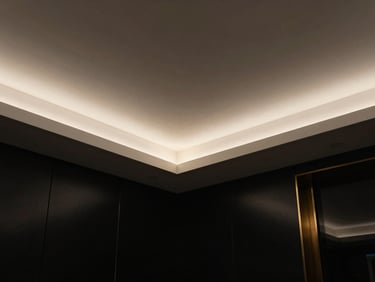 Low-angle architectural photograph of an unbroken monolithic plaster ceiling with recessed warm cove lighting, deep shadows, luxury black backdrop, 35mm