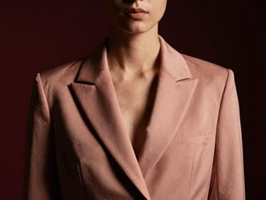 Moody editorial photography of a structured rose-gold toned blazer on a model, dramatic chiaroscuro lighting.