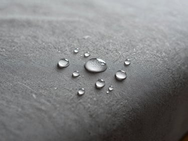 Water droplets pooling perfectly on top of an upholstered fabric surface without penetrating, showing high-performance water repellency.