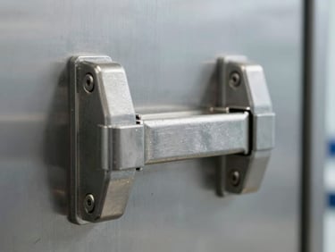 Close-up of industrial heavy-duty door latches on a stainless steel chamber, sharp focus, clinical laboratory lighting.