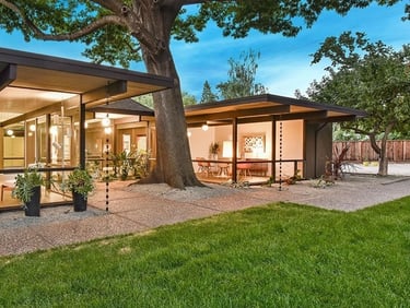 Santa Ynez Valley home with glass walls, flat roof, and a large oak tree in a lush green backyard.