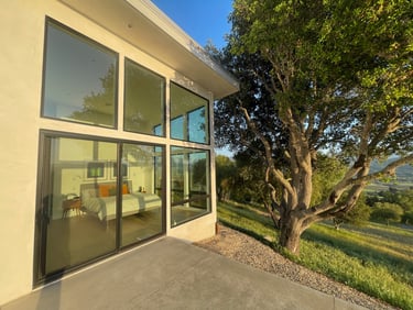 Modern luxury bedroom with floor-to-ceiling glass windows and sliding doors overlooking a lush hillside.